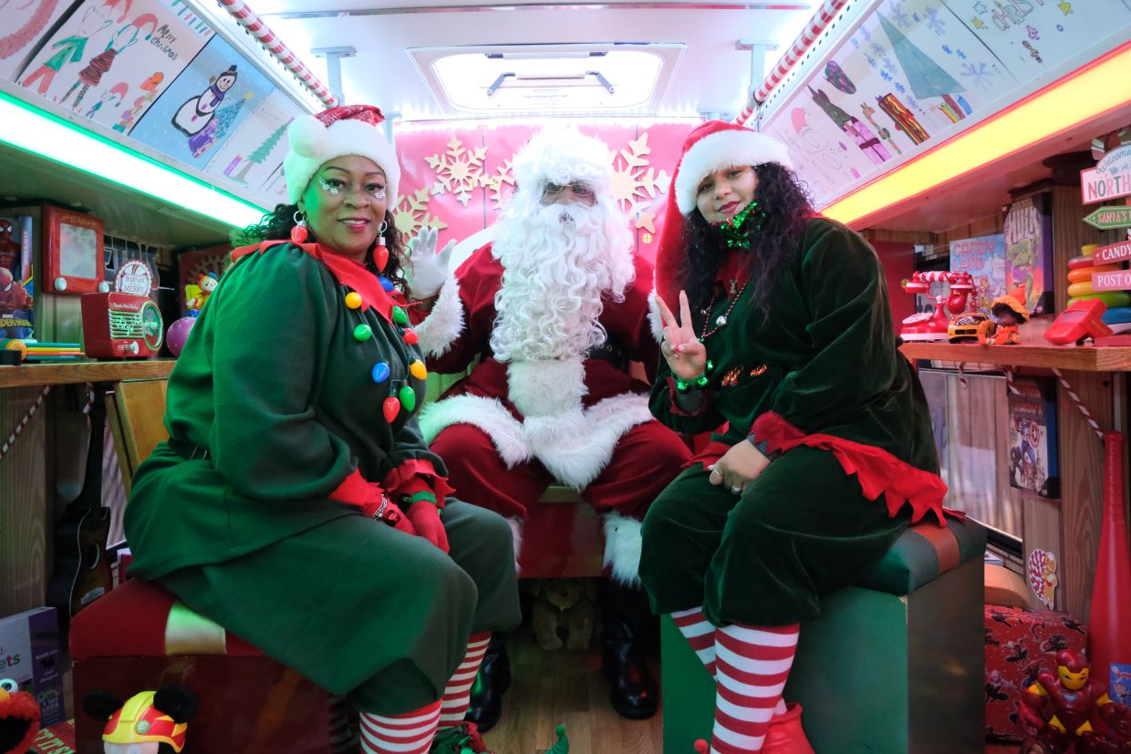Santa and two elves smiling for photo on the holiday bus