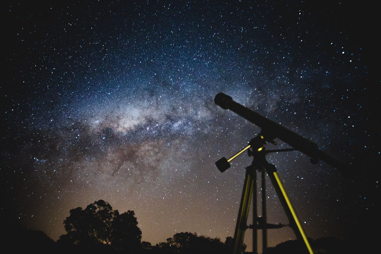 Telescope pointed at night sky with clouds and stars
